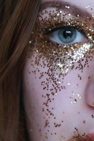 Close-up of a woman's eye adorned with shimmering gold glitter makeup.